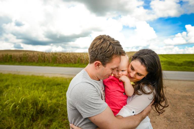 Família feliz, pai, mãe e filha fotografados pelo melhor fotógrafo de Curitiba e Campo Largo, Michel Druziki. Pais abraçados com a filha no campo