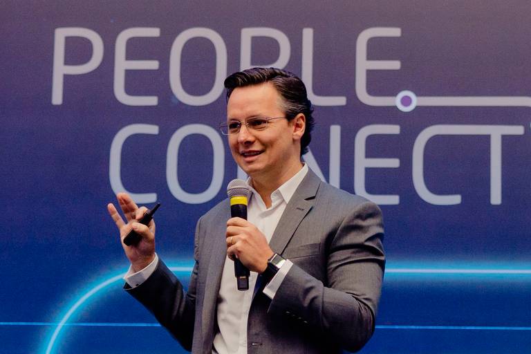 palestrante em evento corporativo em hotel em copacaba rio de janeiro vestindo blazer cinza e camisa social branca segura microfone e sorri para a platéia.