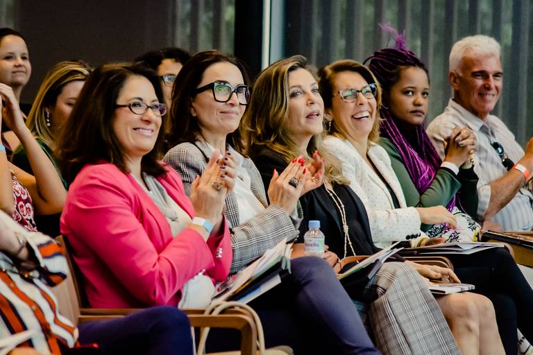 pessoas da platéia de evento corporativo batem palmas para palestrante. todos estão sorrindo.