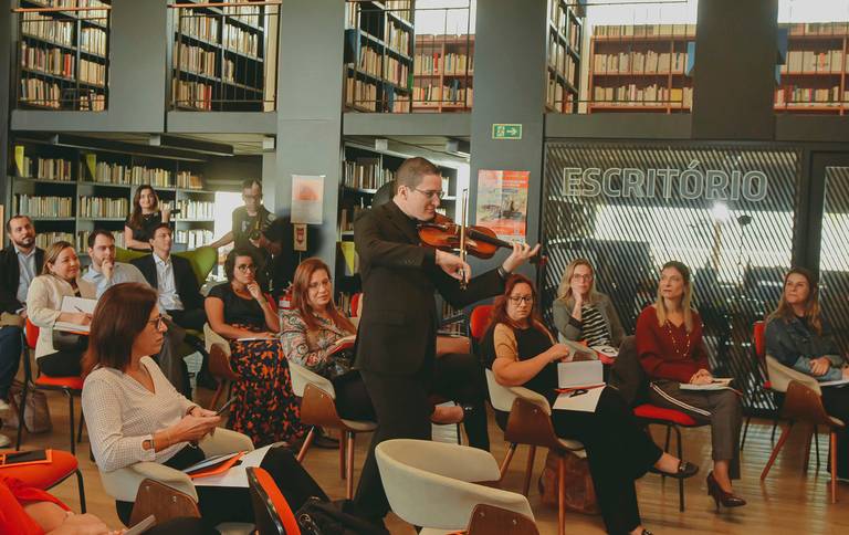 homem de preto tocando violino entra na sala onde ocorrem apresentações em uma biblioteca
