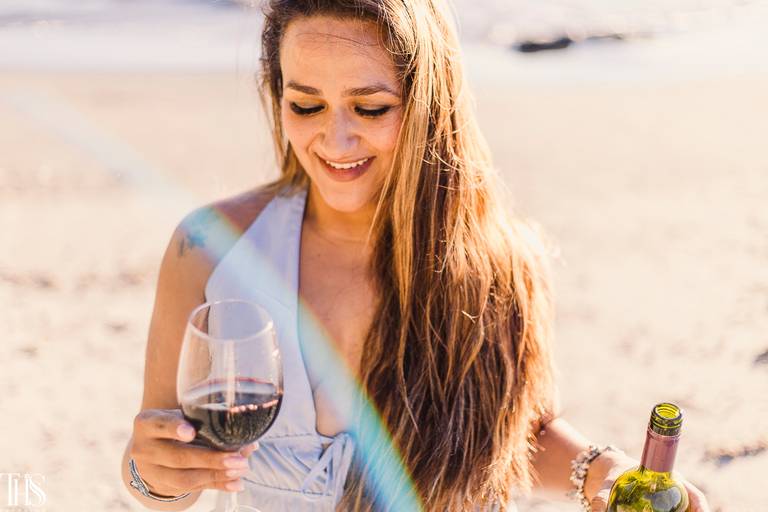 mulher com vinho e taça em mãos na praia ensaio feminino