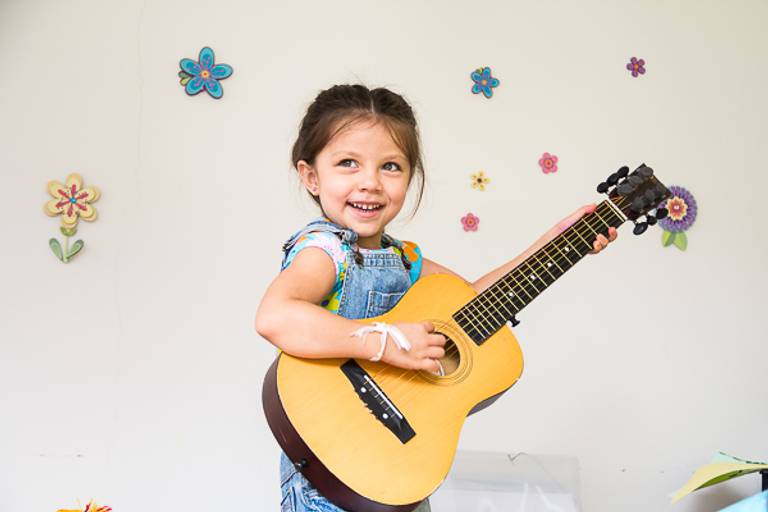 Menina-com-violão-nos-braços-e-parede-com-flores-em-campinas-sp