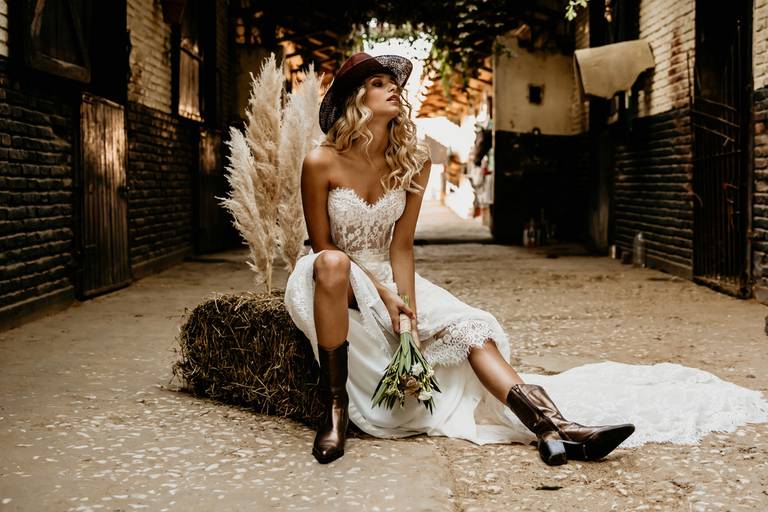 Novia country con botas texanas en hipódromo. Caballos en el stud con vestido de novia. Erika Fayolle