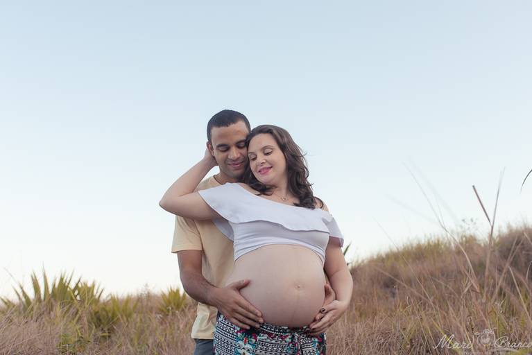 Fotografia de gestante em montanha com céu azul ao fundo na praia da Barra da Tijuca no Rio de Janeiro