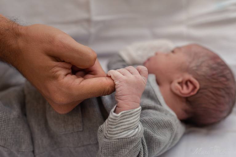 Fotografia de parto cesárea e normal em Maternidade Perinatal Barra RJ. Foto do recém nascido segurando o dedo do pai no berçário