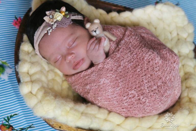 bebe enrolado no wrap com lacinho na cabeca segurando ursinho