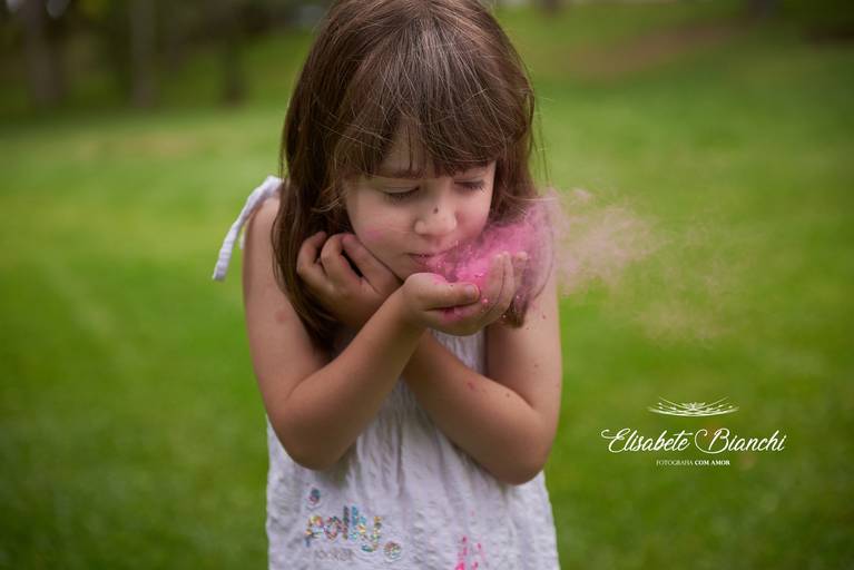 Criança assoprando um pó rosa, em ensaio infantil, em Caxias do Sul.
