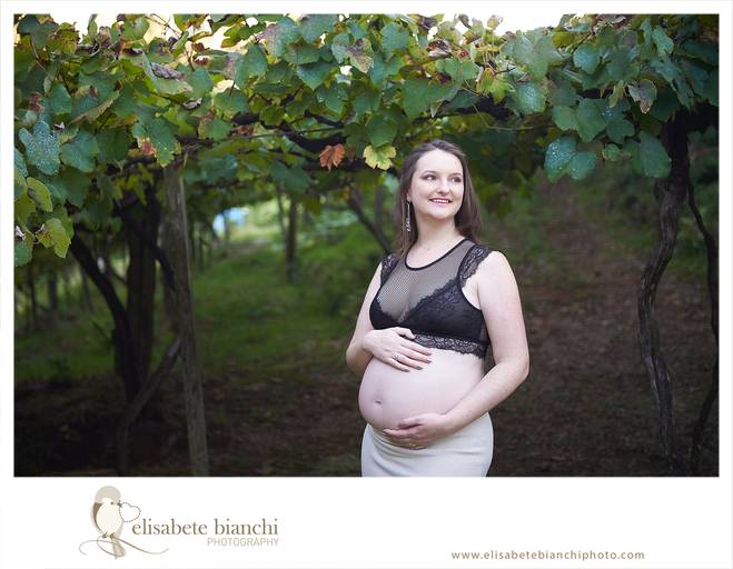 Gestante feliz, acariciando a barriga, em meio a um parreiral, no ensaio externo de fotos da gestação, realizado nas Casas Bonnet, no interior de Caxias do Sul.