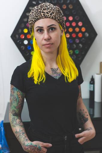 Retrato de mulher tatuadora vestida de preto de cabelo amarelo e boina
empreendedora tatuada Santa Helena - PR