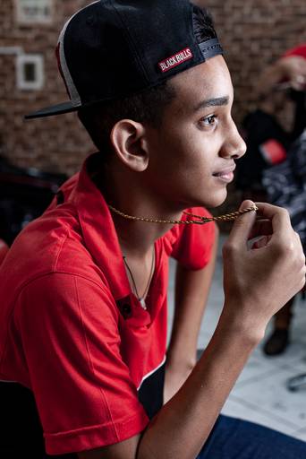 retrato lateral de garoto negro barbeiro e cabeleireiro de camiseta vermelha segurando um colar de ouro