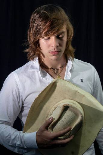 Retrato feito em estúdio de homem de cabelo castanho e camisa branca segurando chapéu de olhos fechados fazendo uma oração. Alan Ten Caten, integrante da dupla Alan Jr. e Marcelo de Santa Helena e Missal - PR
