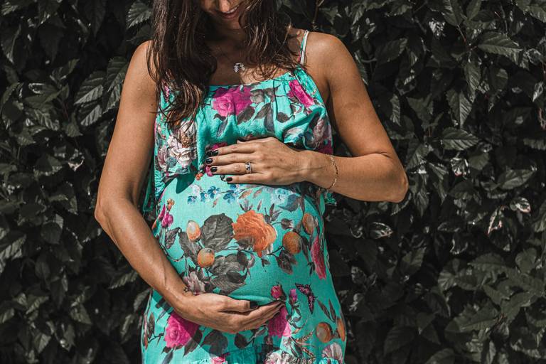 Grávida no jardim com as mãos na barriga