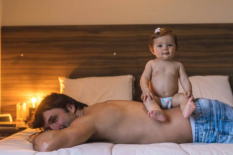 menina sentada nas costas do pai deitado na cama

