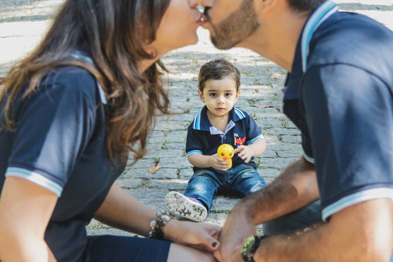 pai e mãe se beijando e filho bebê olhando