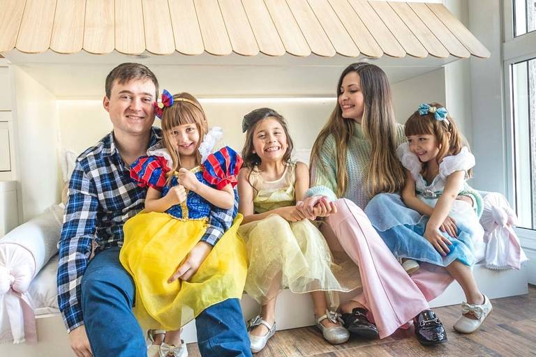 Família sentada na cama com meninas de fantasia das princesas