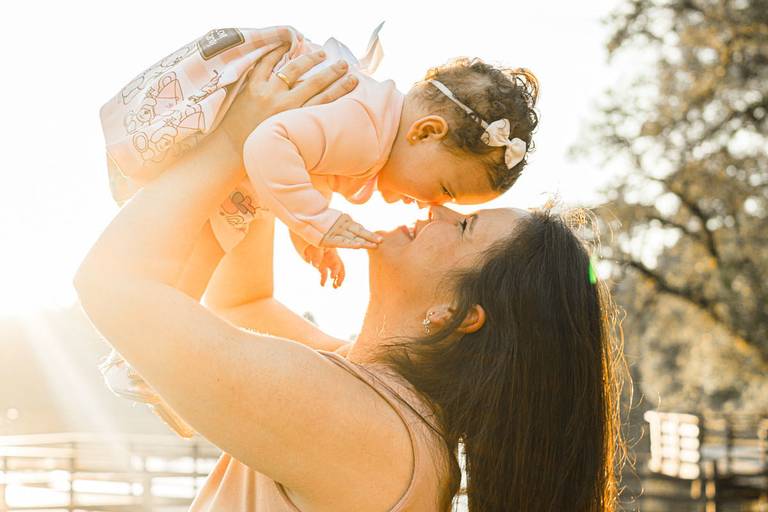 Mãe levantando filha no alto no Parque Lago Azul em Curitiba ao pôr do sol 