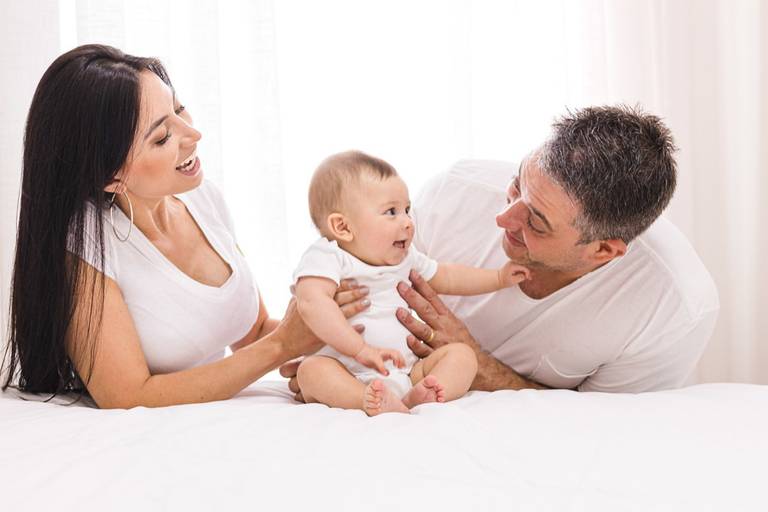 Pai, mãe e filho bebê brincando na cama