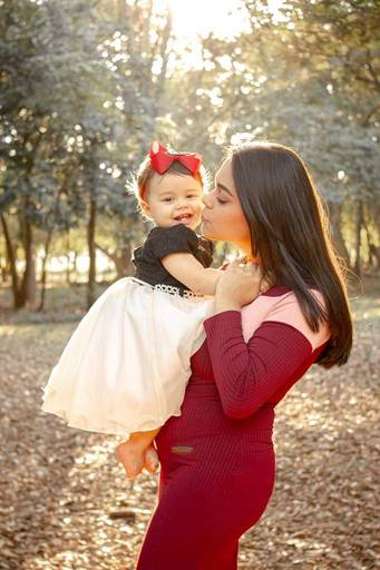 Mãe beijando a filha bebê no pôr do sol no parque 