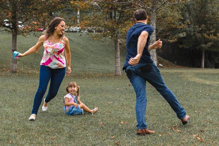 Mãe e pai brincando e correndo com a filha no parque Tanguá em Curitiba 