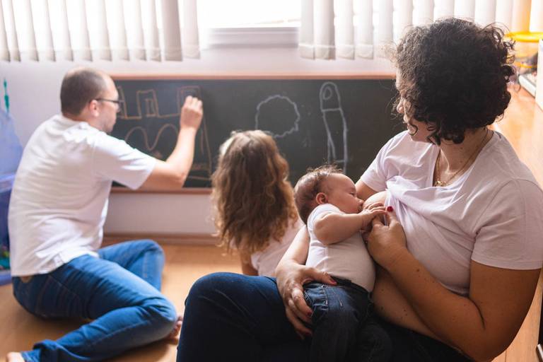 pai desenhando com a filha no quadro negro e mãe amamentando bebê