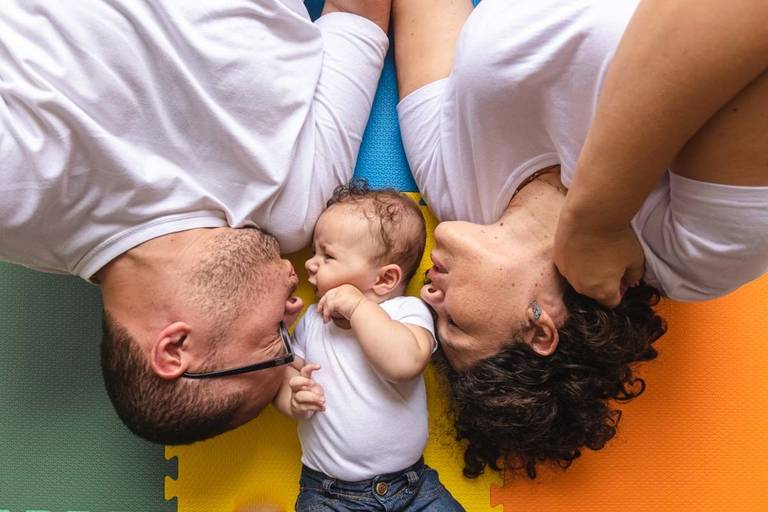pais beijando bebê deitados no tapete colorido  chão 