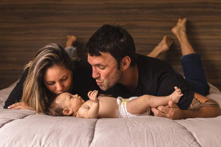 pais deitados na cama brincando com bebê de 3 meses