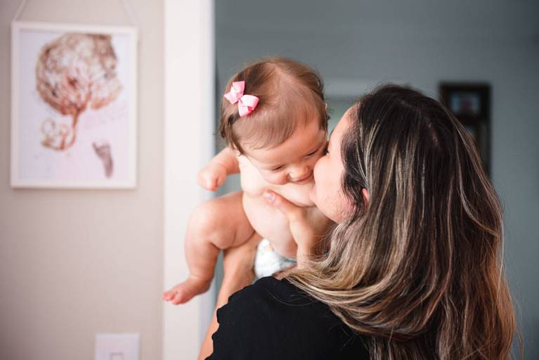 mãe brincando com filha no colo no quarto