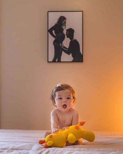 bebê sentada na cama com foto dos pais na parede