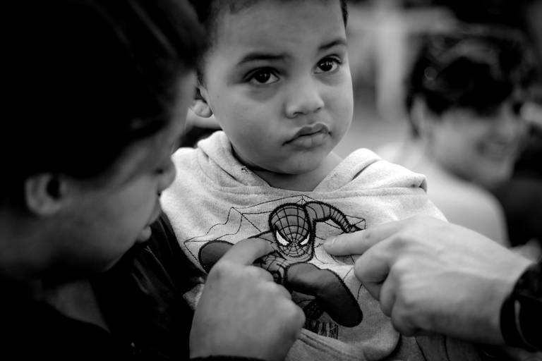 foto retrato  preto e branco do pais de uma criança  de colo apontando na camisa dela o homem aranha