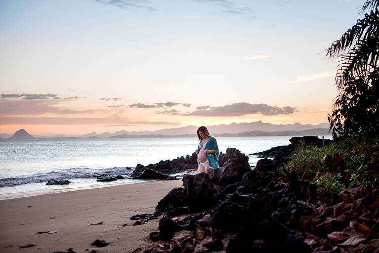gestante no meio das pedras na praia durante sua sessão de fotos