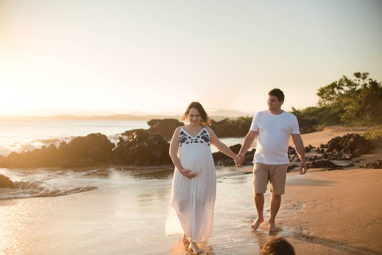 casal andando de mãos dadas na praia durante sessão de gestante