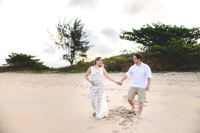 gestante e seu marido correndo na praia de mãoes dadas durante o book de gestante