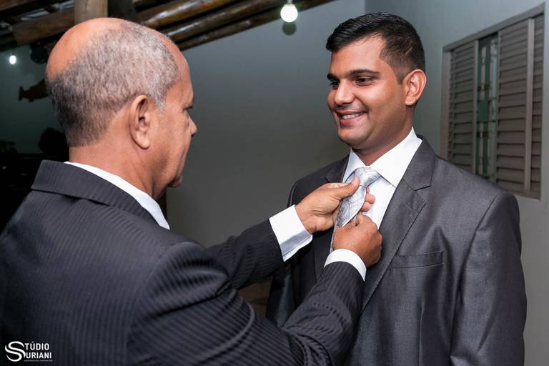 Noivo sendo arrumado pelo pai antes de se casar com gravata cinza 