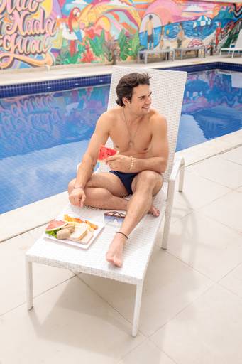 fotografia publicitária para banco de imagens jovem com roupa florida sentado com drink amarelo laranja na beira da piscina pelo fotógrafo paulo henrique lima em hotel no recreio rio de janeiro rj